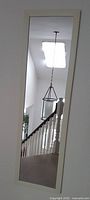 Full length mirror in white frame showing reflection of stairway and ceiling light fixture.