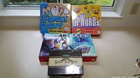 Four games arranged together: Family Guy Trivia Game in a blue tin, Upwords game in yellow box, Break the Safe game in large box, Shut the Box in wooden styled box.