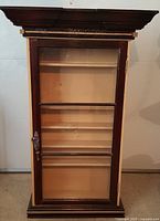 Front view of the vintage wooden glass display cabinet with door closed showing decorative molding.