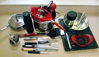 Photo showing all kitchen accessories on a white table including stainless cooking pot, UV water bottle, knives, and various utensils.