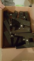 Box of black metal sawhorse brackets showing several units stacked inside a cardboard box.