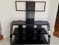 Front view of the black glass and metal TV stand showing the three shelves and mounting bracket.