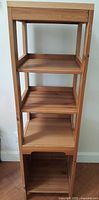 Straight front view of the wooden shelving stand showing four shelves and a bottom compartment.