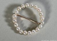 Top view of circular brooch with white cultured pearls on gold frame, showing pearls and bent pin arm.