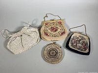 Lot overview showing four vintage handbags including a cream-colored drawstring bag, a white floral embroidered purse, a round beaded lace clutch, and a black needlepoint purse.