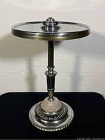 Front view of the 1930s Art Deco MetalCraft accent table showing the circular metal top with central knob, tapered stem, and decorative base with pink marbled stone detail.