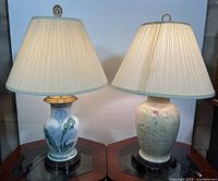 Pair of vintage chinoiserie table lamps lit, showing bases with floral motifs and pleated fabric shades