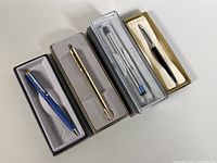 Four vintage pens in original boxes: Sheaffer blue pen, gold-tone Parker pen, clear Parker mechanical pencil with eraser, black Parker pen.