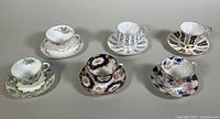 Six assorted bone china teacups and saucers displayed in two rows showing different patterns and designs.