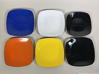 Top view of six square enamel plates in blue, white, black, orange, yellow, and black colors.
