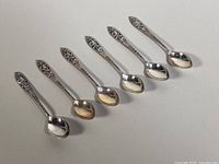 Photo of six sterling silver Bermuda collector spoons arranged in a row, showcasing ornate floral handles and polished bowls.