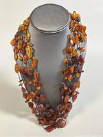 Front view of the 8-strand amber necklace displayed on a grey bust stand, showcasing the beads and layering effect.