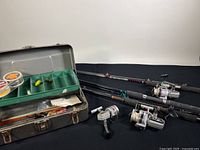 Overview of three fishing rods, three reels, and open tackle box with lures and line inside