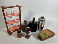 Wide view showing entire lot including shot glasses on stand, flasks, cocktail picks holder, wooden toothpick holder, and wooden trays with felt.
