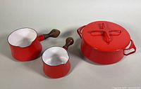 Set of three enamel pots: one large covered pot and two smaller sauce pots with wood handles, showing overall good condition and bright red color.