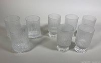 Eight clear textured highball glasses arranged in two groups - the three Ultima Thule glasses are shorter and wider, the five Aslak glasses are taller and more cylindrical.