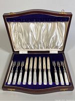 Wooden case open displaying six mother-of-pearl handle knives and forks on velvet lining