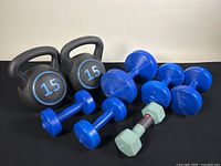 All items in the lot displayed on black surface showing two kettlebells, multiple blue dumbbells of various sizes, and one green hex dumbbell.