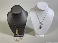 Photo showing the 16 inch cord choker with gold-tone clasp and faceted crystal pendant, the white gold-plated heart necklace on display busts, and matching drop earrings laid flat
