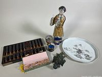 Full lot showing wooden abacus, porcelain figurine, decorative plate, carved figure, two small cups, and mala beads in open box on table