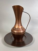 View of the hammered copper jug placed on the matching hammered copper plate showing the texture and patina.