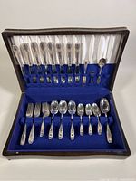 Full set of vintage McGlashan silver plated flatware displayed in an open wooden chest with blue and white velvet and satin lining.