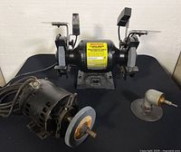 Wide shot of Workforce bench grinder with two grinding wheels, additional black motor with grinding wheel, and small angled grinding attachment on a black surface.