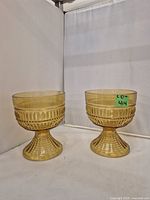 Pair of amber-colored glass pedestal bowls viewed from front showing ribbed texture and patterning.
