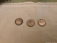 Top side view showing the reverse with the centennial logo and various animals on the three coins, placed side by side on a white cloth.