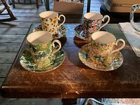 Four Royal Albert demitasse cups and saucers arranged on a wooden table. Each set has different vibrant floral patterns.