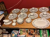 Overview of dinnerware set on table showing 8 place settings including plates, cups, saucers, and multiple serving pieces.