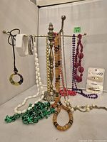 Multiple costume jewelry necklaces and earrings displayed on vintage-style metal jewelry rack with floral base and twisted arms.