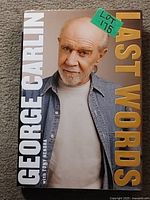 Front cover of the book 'Last Words' featuring a large photo of George Carlin with a denim jacket and white shirt, title and author text.