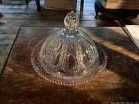 Clear vintage glass butter dish with bubble bead decoration on the rim, dome lid with a decorative knob handle shown on a wooden table.