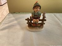 Front view of the Way Side Harmony Hummel figurine showing the boy seated on the fence with bird.