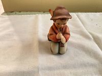 Front view of the Hummel Little Tooter figurine kneeling while playing a horn.