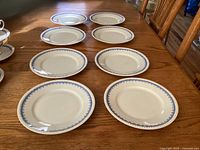 Eight white salad plates with blue floral border arranged on wooden table.