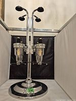 Full view of a chrome dual liquor bottle dispenser with two pouring mechanisms and two bottle insertion points on a weighted base