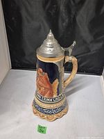 Full view of the front of the lidded German beer stein, showing relief artwork of men drinking and decorative text.