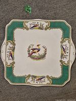 Front view of square ceramic platter with green border and colorful bird artwork.