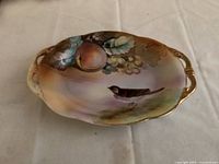 Top view of Nippon oval serving dish with hand painted bird, peach, grapes, and leaves in pastel colors, gold trim and handles.