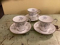 Three Paragon Brides Choice teacups and saucers arranged on a rustic green wooden surface, showing the pattern and silver trim on the rims and handles.