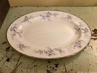 White oval porcelain platter with light blue floral design and gold trim, placed on a rustic wooden surface.
