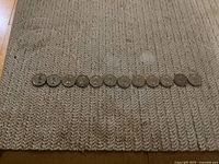 Obverse side showing 12 Canadian nickel coins featuring Queen Elizabeth II Young Head design, arranged in a line on a knitted fabric surface.