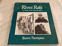 Front cover of 'River Rats' book by Shawn Thompson showing title, author, and three black and white images: boathouses on water, man wearing 'Muskie Jake' baseball cap, and a stone building.