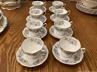 Eight tea cups with matching saucers arranged on table showing delicate silver maple leaf pattern and gold trim on edges