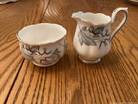 Cream pitcher and sugar bowl set on wood table showing pattern and shape.