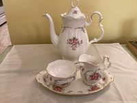 Photo showing coffee pot, creamer, sugar bowl, and tray on a white cloth background showcasing the floral and gold trim design