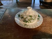 Covered butter dish with white trillium flowers on top of matching scalloped bread plate