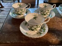 Three Royal Albert Trillium tea cups arranged on matching saucers on a table, showing the floral design and the shape of the cups.